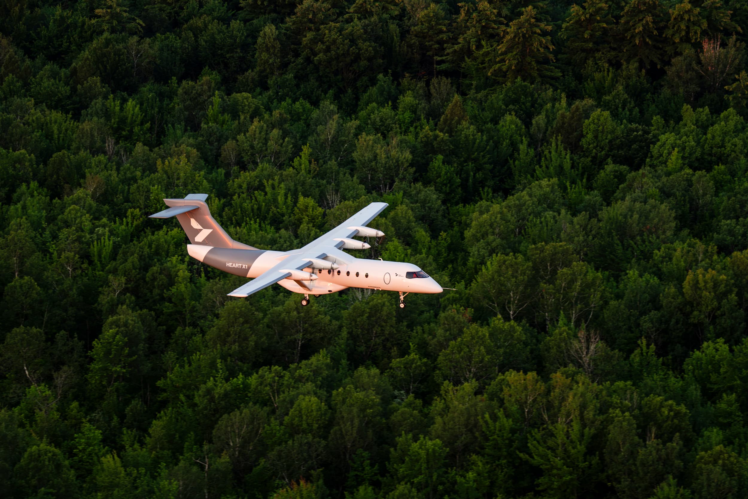 Heart Aerospace’s X1 battery-electric demonstrator flies above dense green woodland.